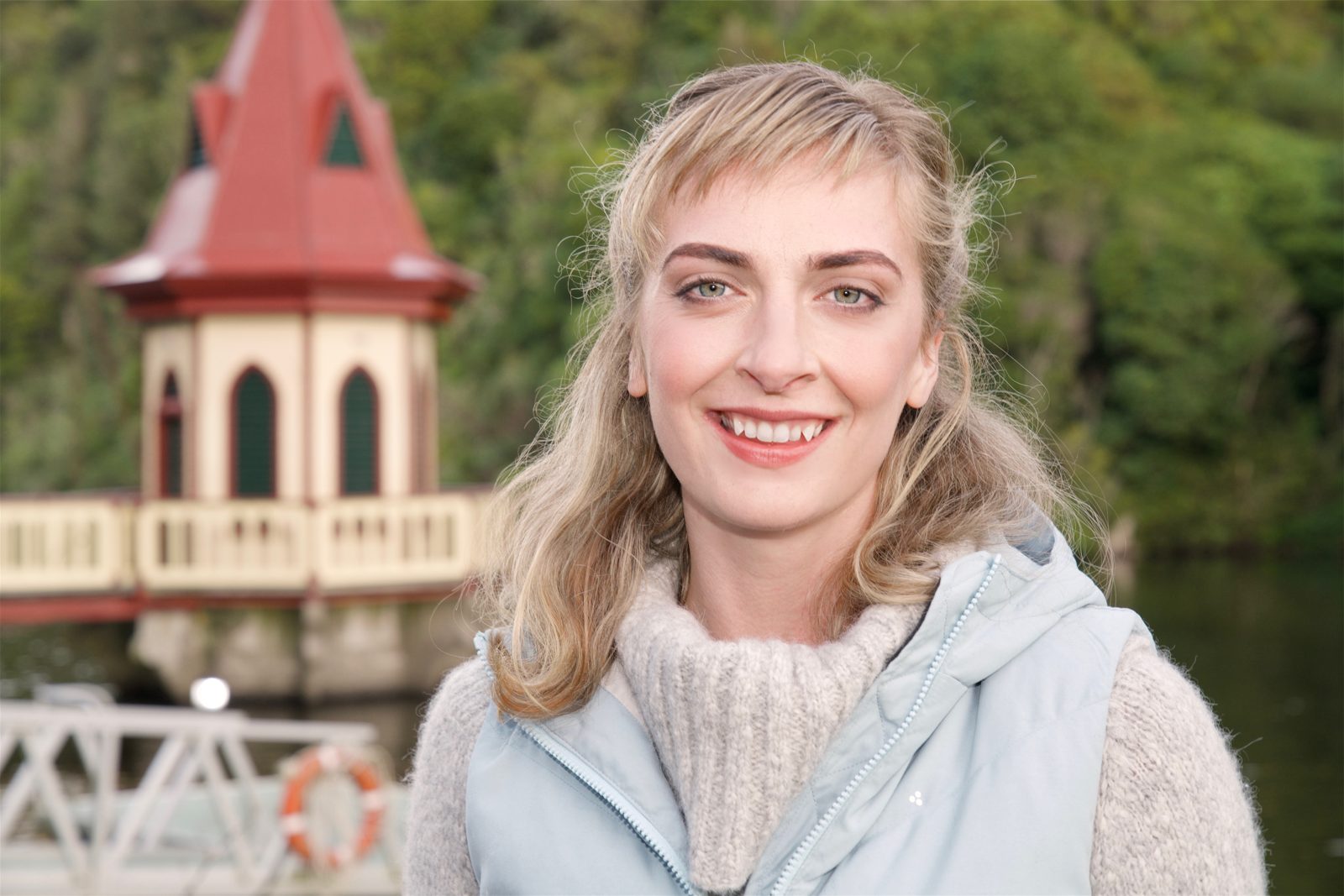Emily Riedel by a lake with a red-roofed tower behind her